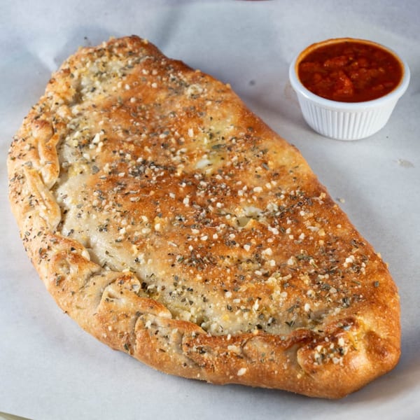 A golden-brown Babe's Pizza calzone, sprinkled with herbs and cheese, with a side of marinara sauce.