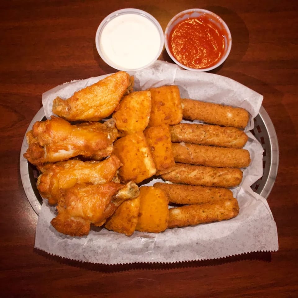 A basket of Babe's Pizza fried appetizers, including wings, mozzarella sticks, and fried ravioli, with dipping sauces.
