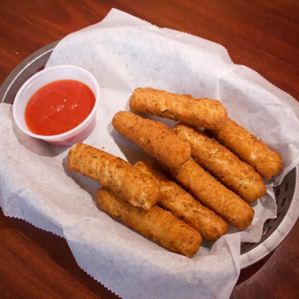 Golden-brown mozzarella sticks in a basket with white paper, served with a side of red dipping sauce.