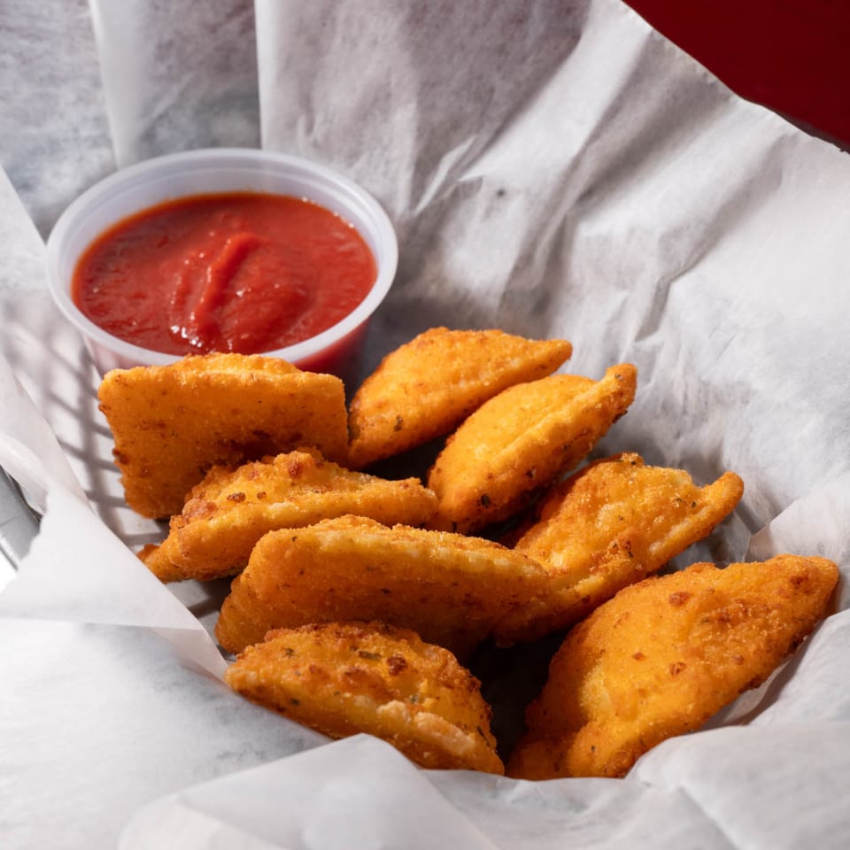 Golden-brown fried ravioli, served in a basket lined with white paper, with a side of red marinara sauce.