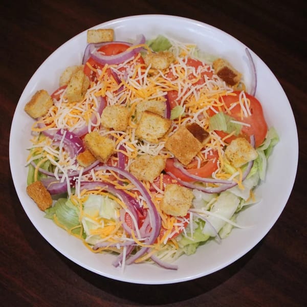 A fresh side salad with lettuce, tomatoes, red onions, shredded cheese, and croutons in a white bowl.