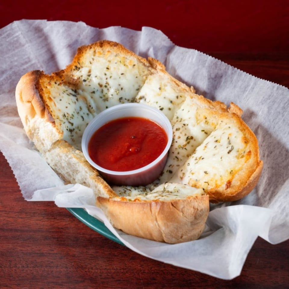 Cheesy garlic breadsticks with herbs and a side of marinara sauce in a basket.