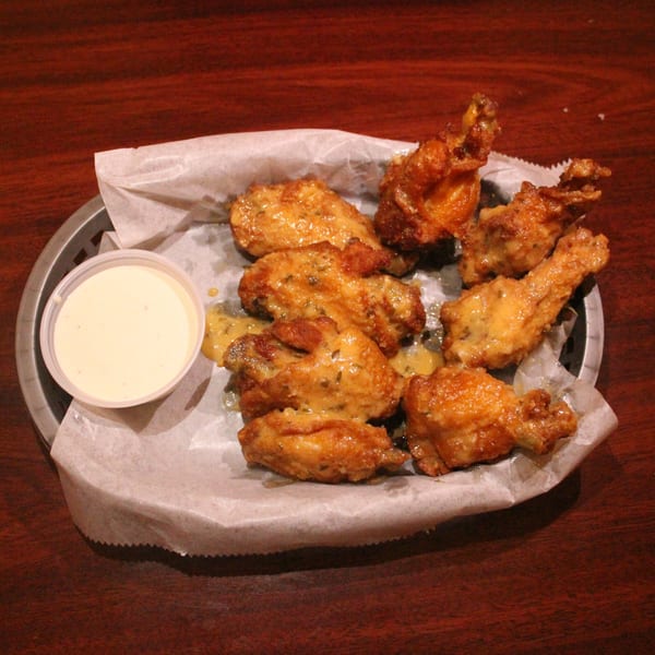 A basket of Babe's Pizza's golden-brown chicken wings with a side of dipping sauce.