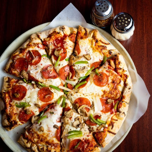 Babe's Pizza with pepperoni, mushrooms, green peppers, and onions, with shakers of spices.